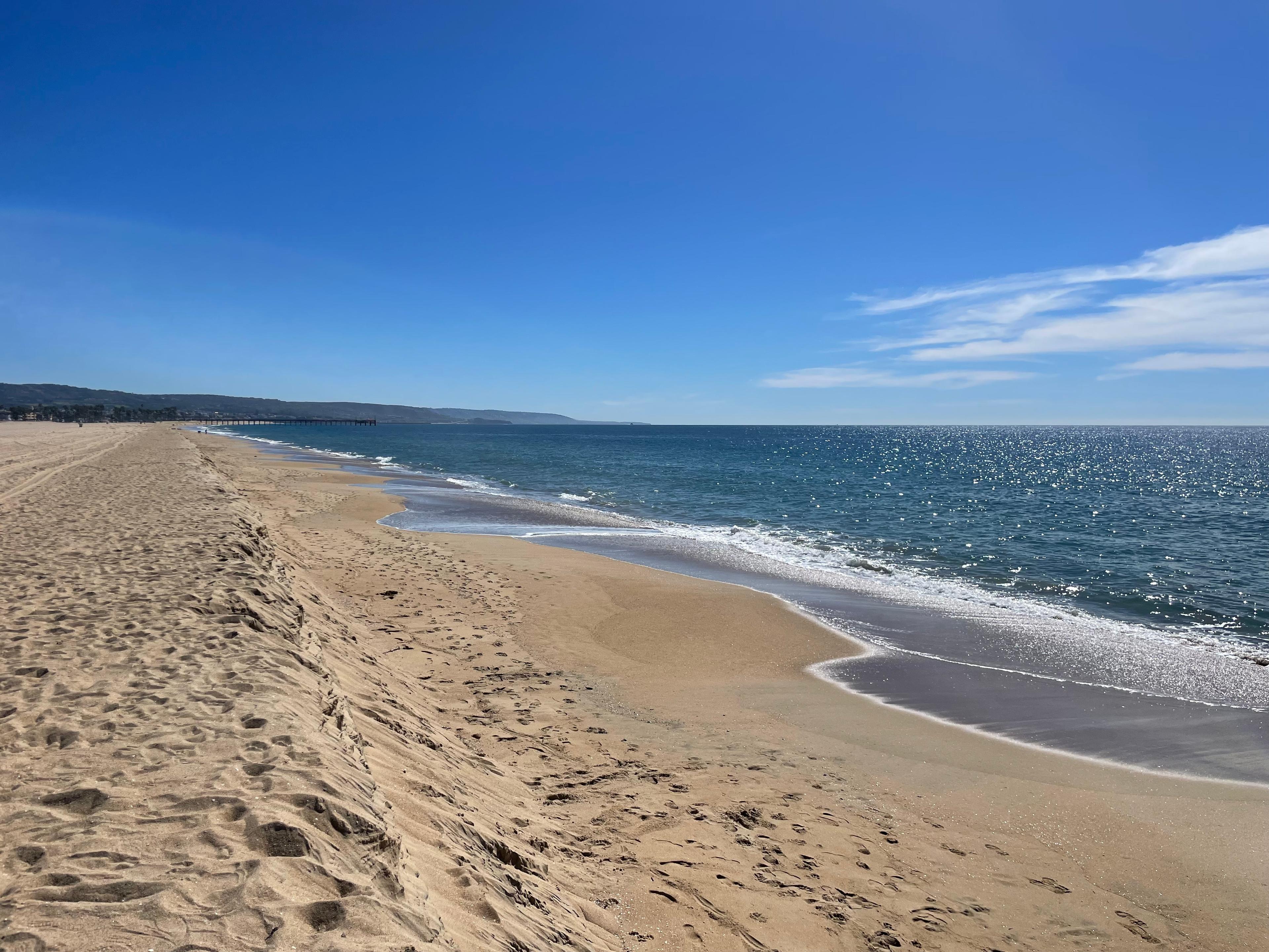 A wide, empty Southern California beach with footprints in the sand and calm ocean waves