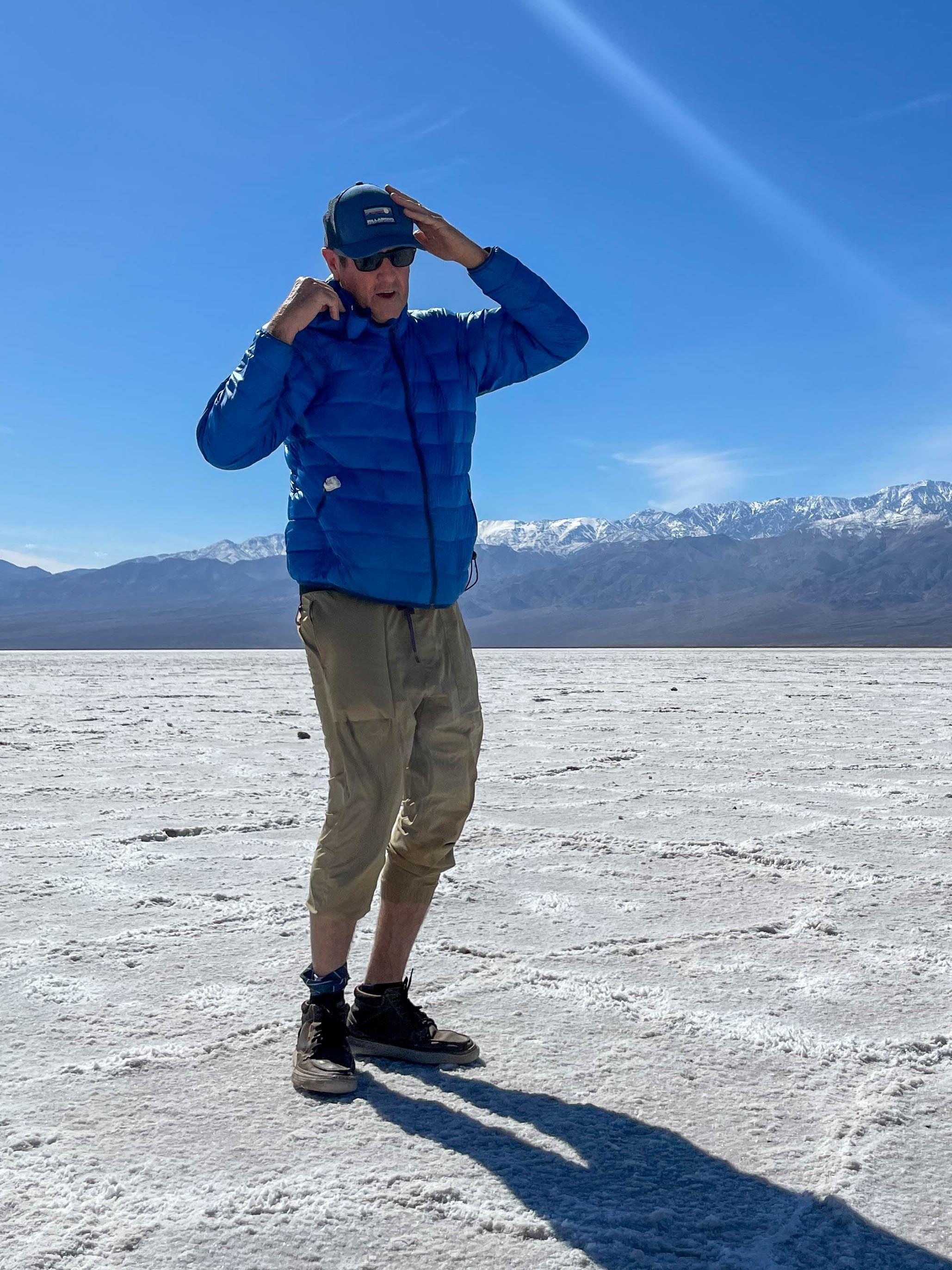 Founder Scott Swift standing on a desert salt flat, shielding his eyes, with snow-capped mountains on the horizon behind him