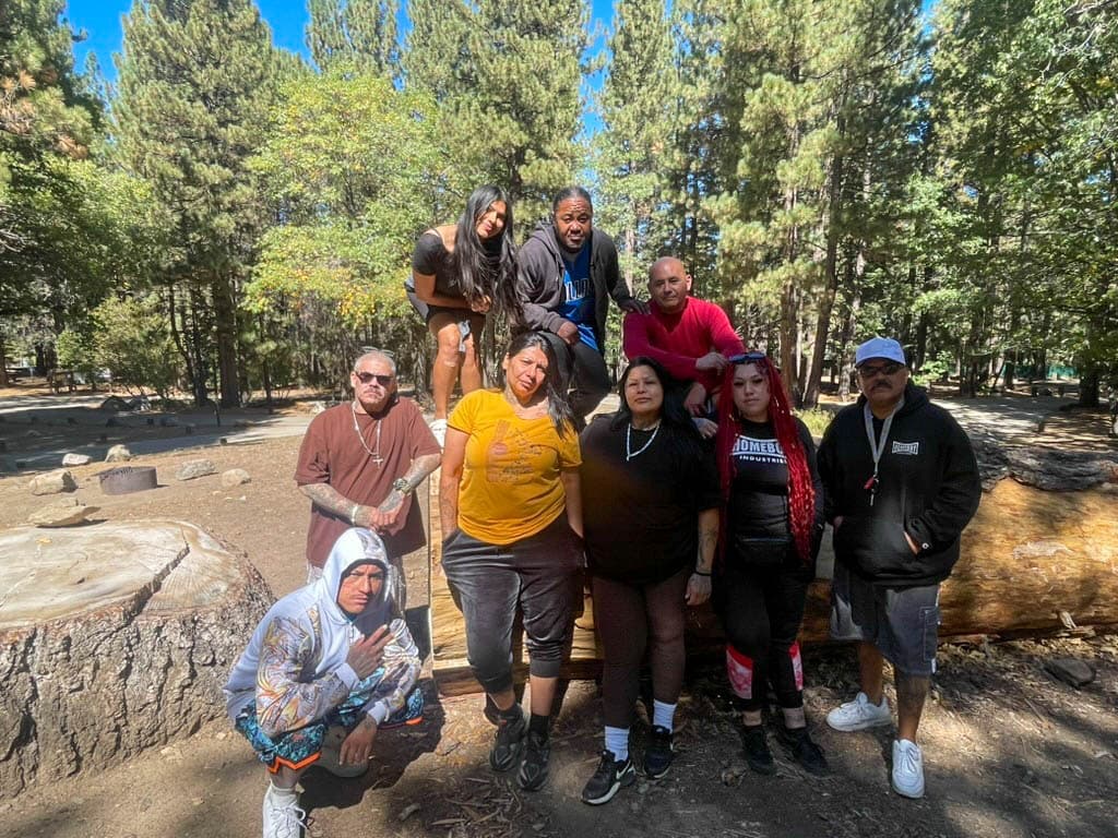 A group of participants posing together around a fallen log at a pine-forest campground in Big Bear