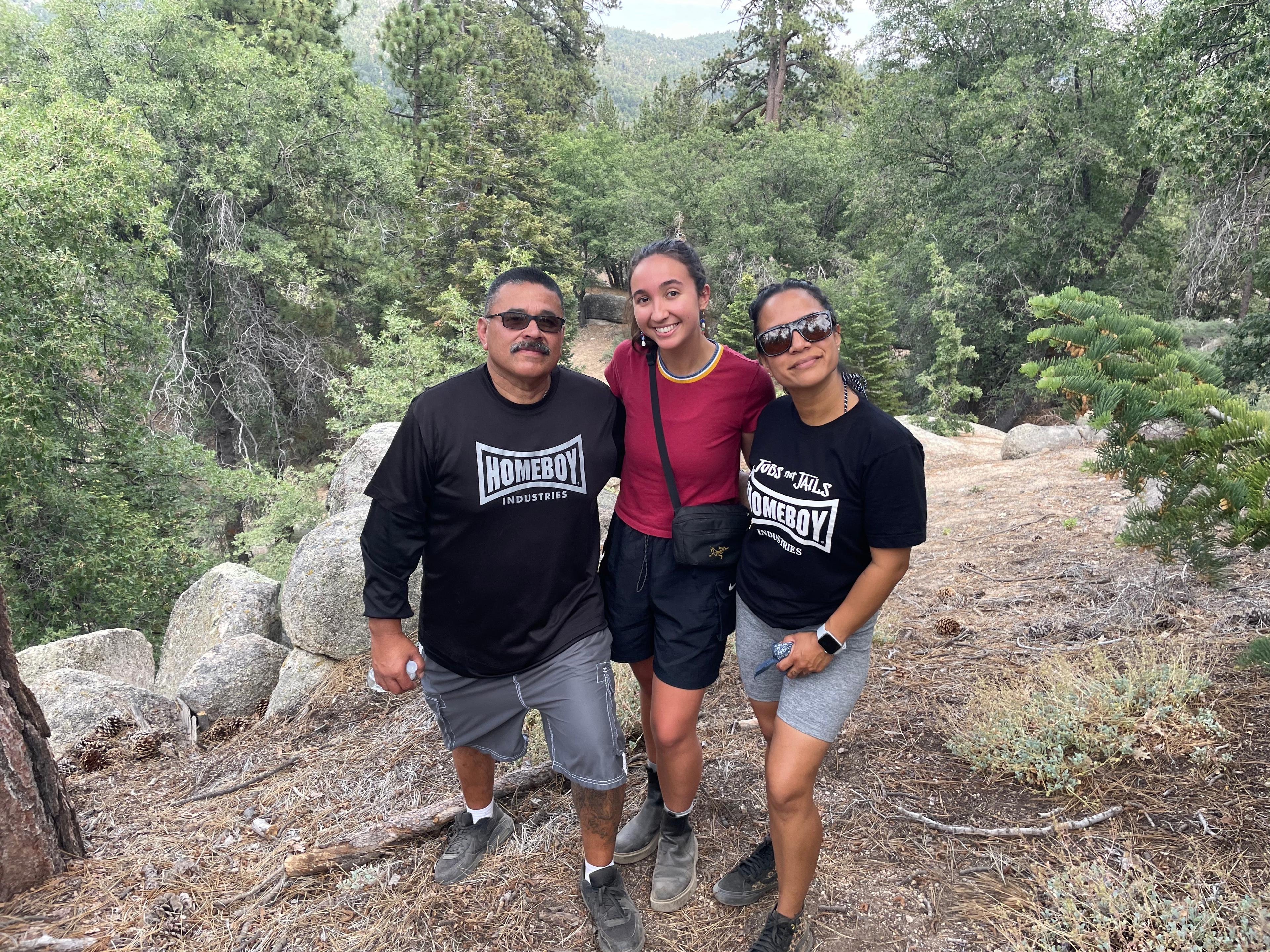 Three hikers smiling together on a trail among boulders and pine trees