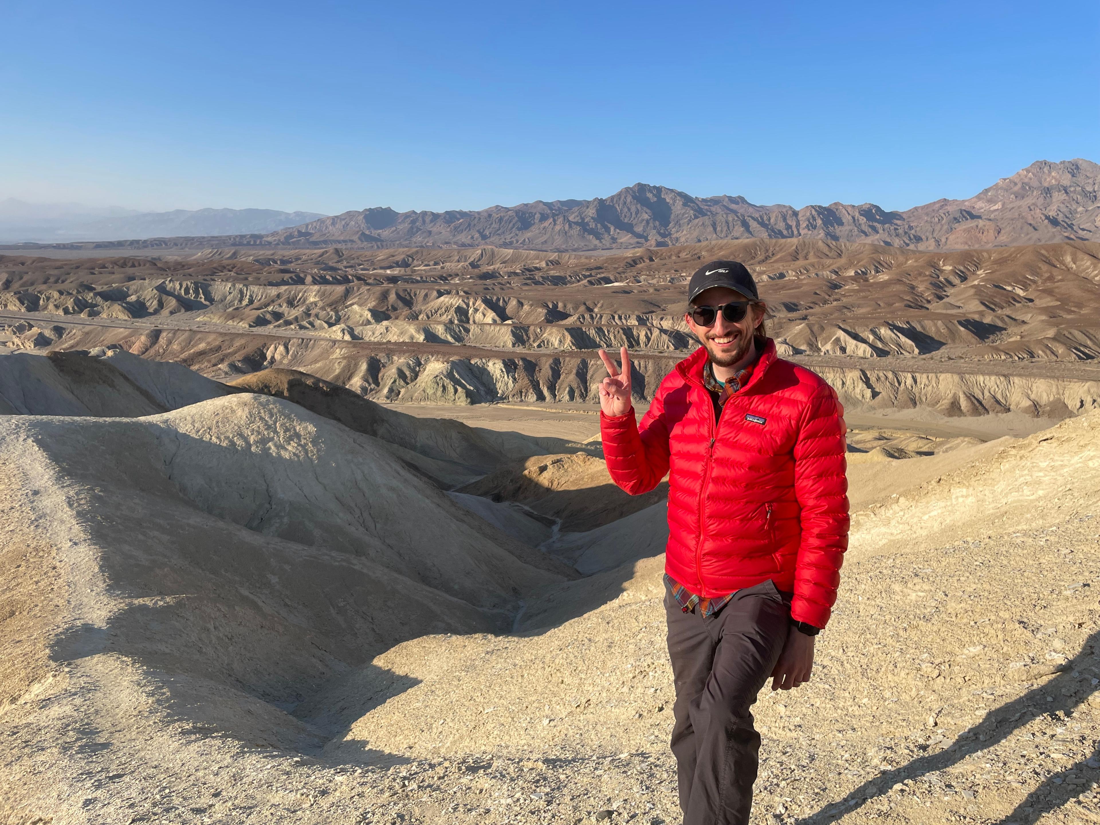 Outside the City's Corey Swift flashes a peace sign above the eroded badlands of Death Valley, with mountains behind