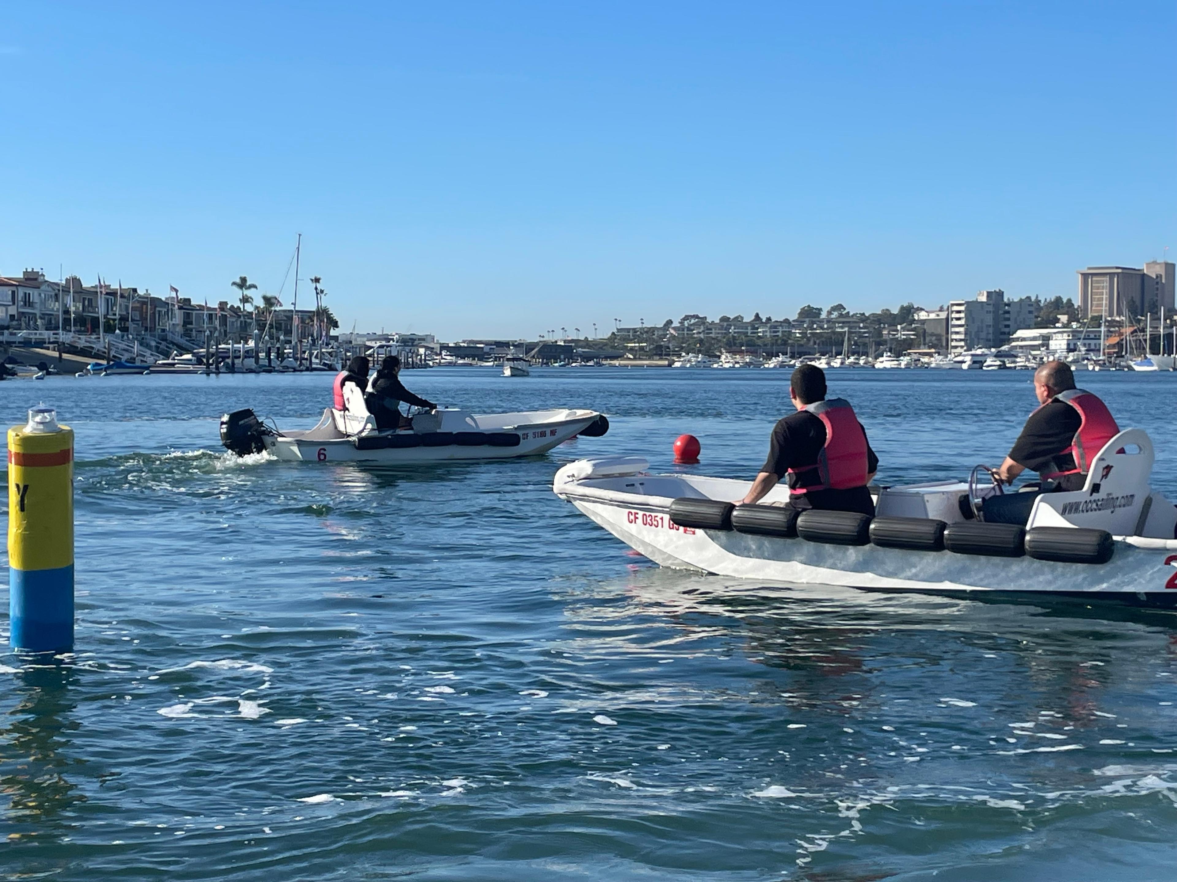 Participants in life vests drive small training powerboats across Newport Harbor
