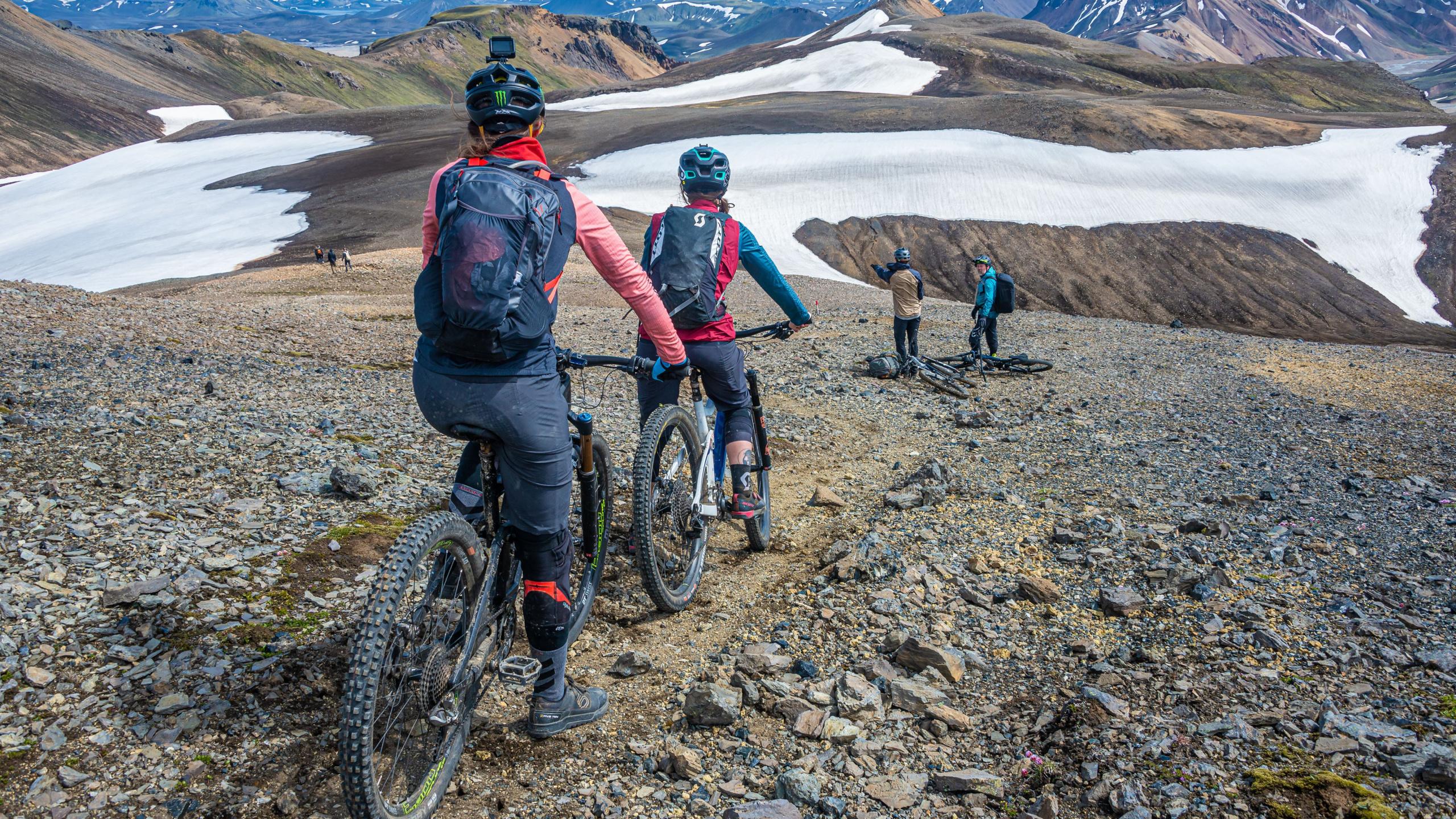 Mountain bikers ride a rocky ridge trail past snowfields in the mountains of Iceland